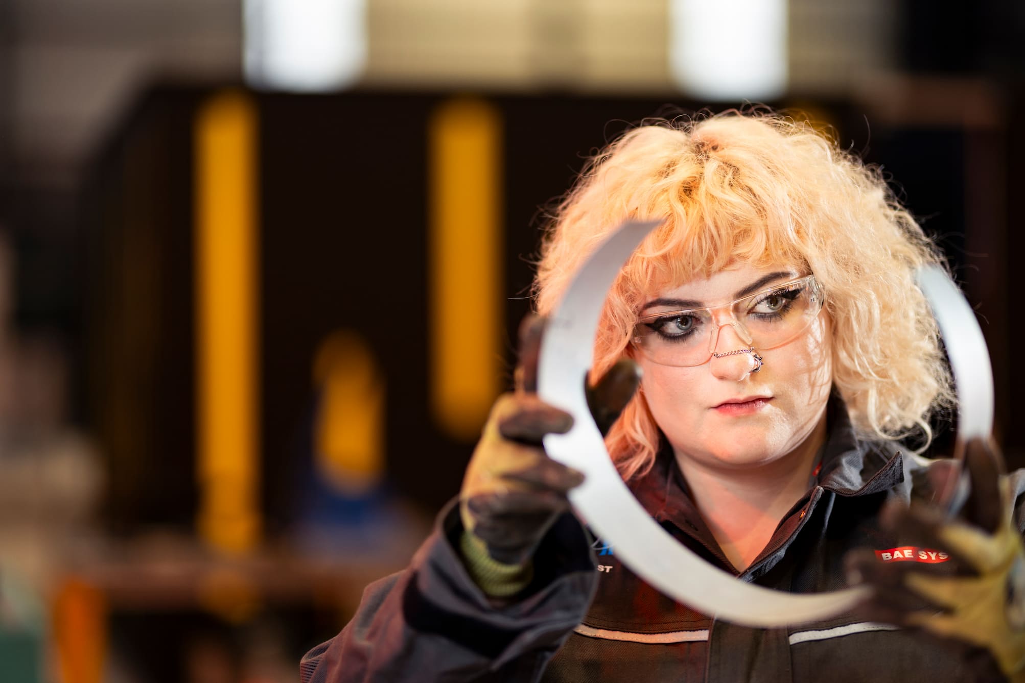 Young woman wearing glasses peering at a piece of cut metal