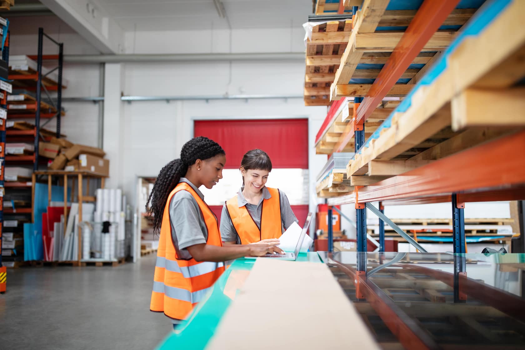 Two women in hi-vis gear looking at plans in a warehouse full of pallets