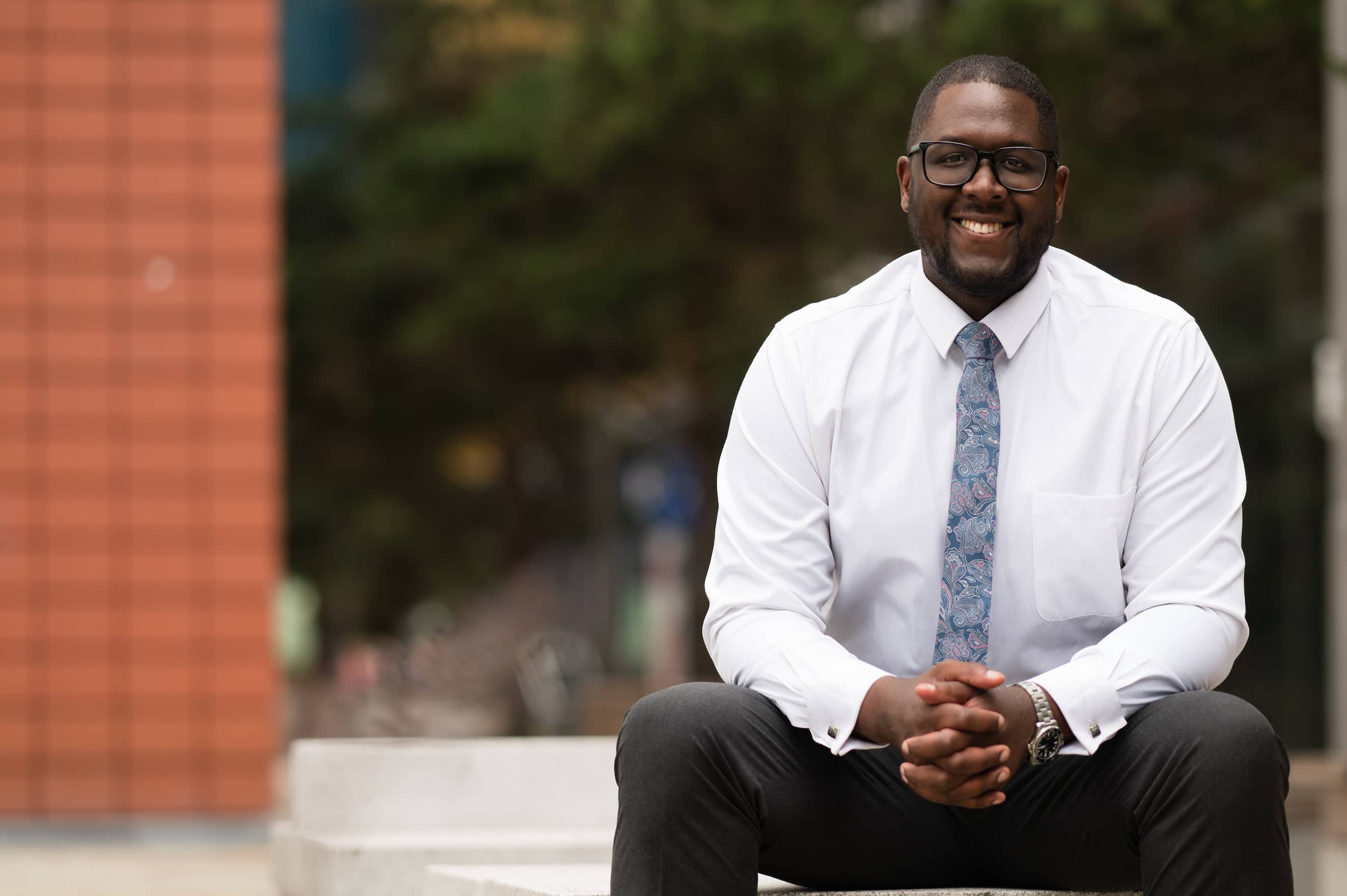 Smiling man dressed in smart clothes sat on a bench