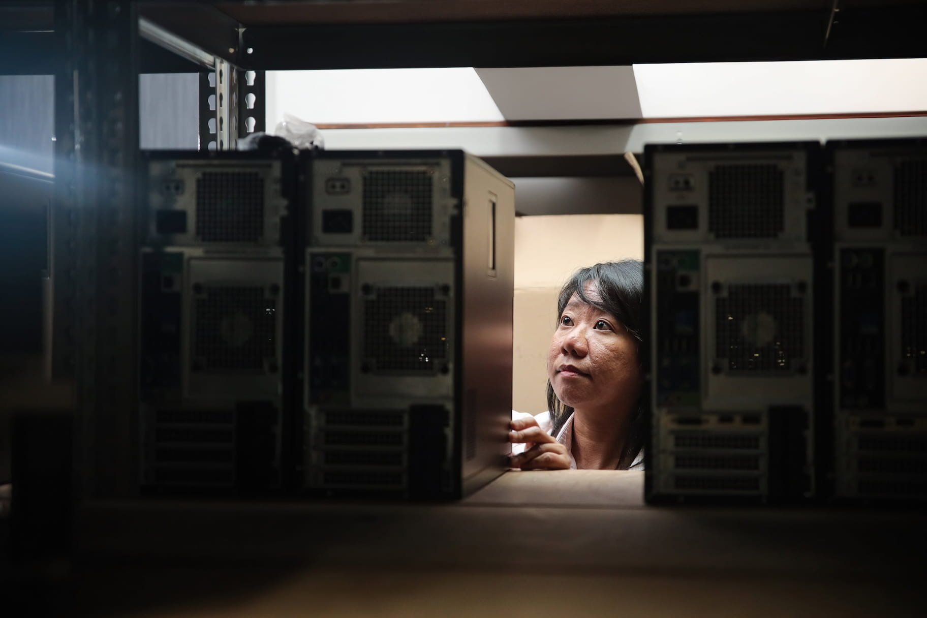 Woman's face peeking between computer towers on a shelf