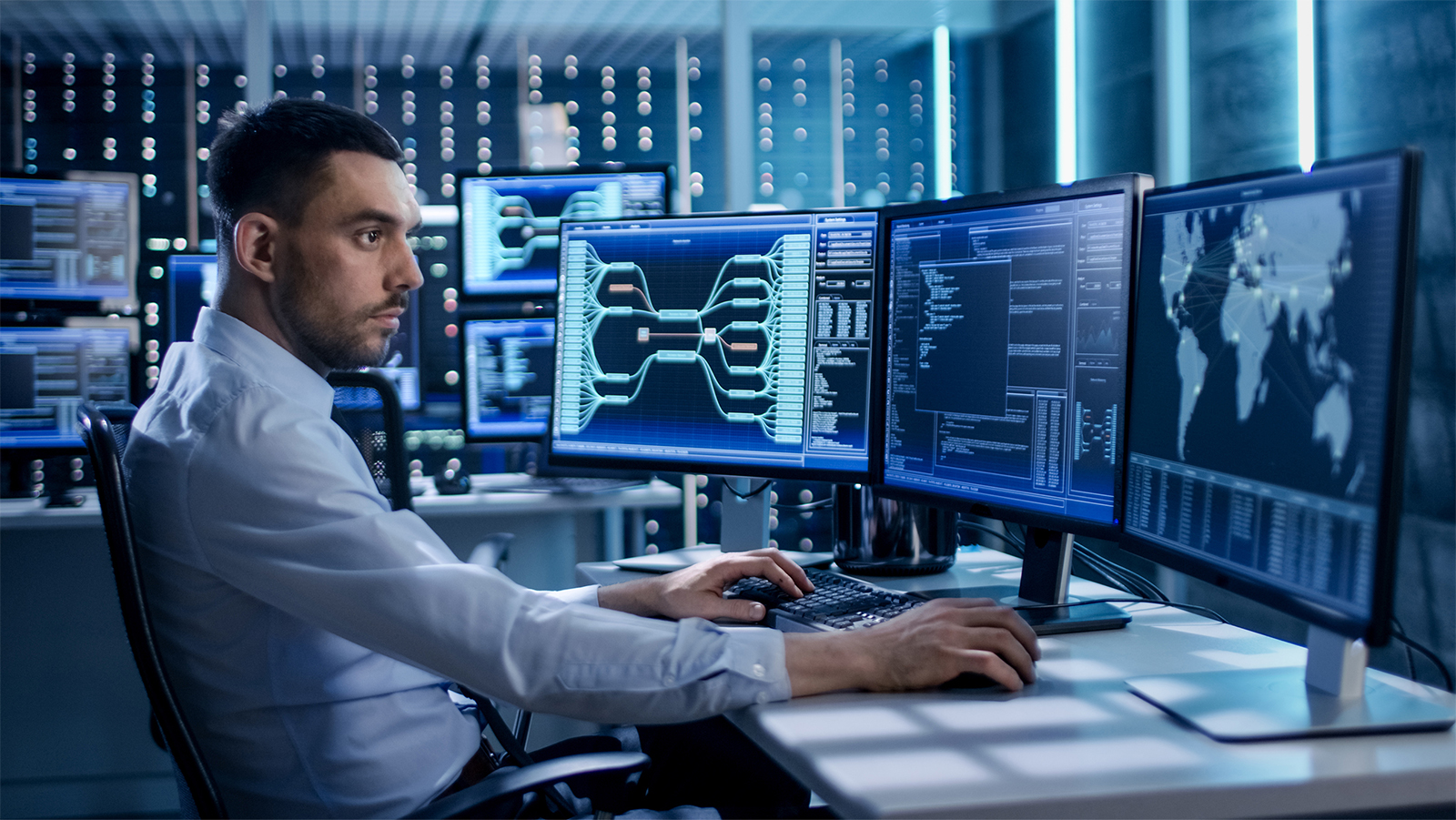 System Security Specialist Working at System Control Center. Room is Full of Screens Displaying Various Information.