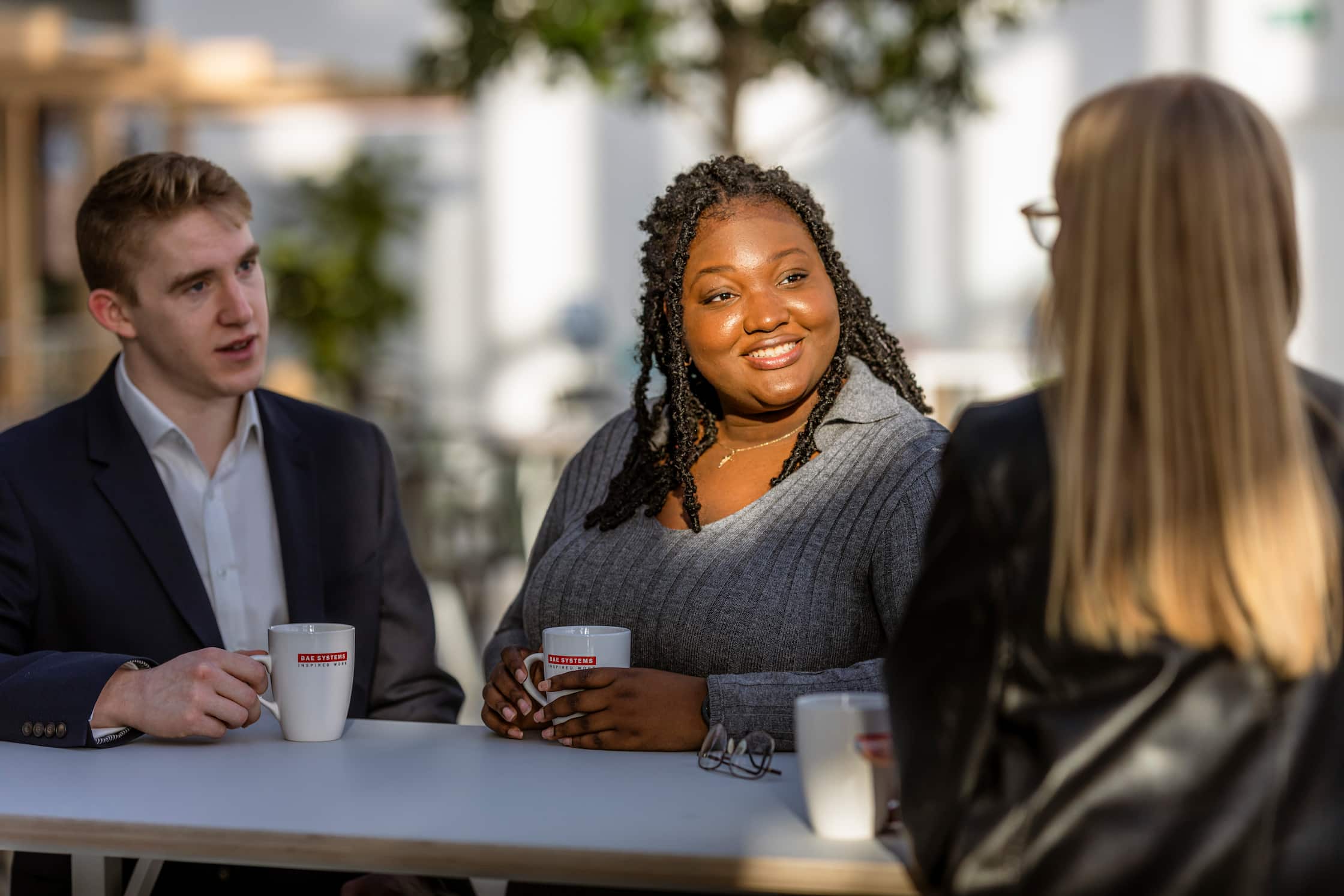 Colleagues with hot drink mugs talking around a table in the outside sunshine